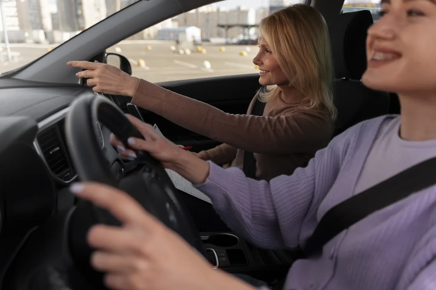 Dos mujeres en los asientos delanteros de un coche; una señala hacia el exterior